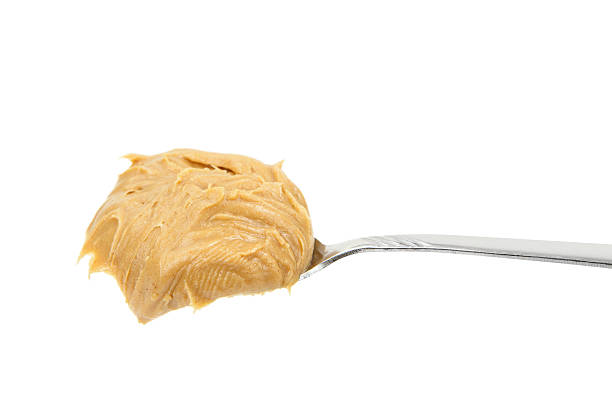 Close-up of creamy peanut butter spread with a rich, smooth texture. The golden-brown surface has visible swirls and ridges, showcasing its thick and glossy consistency.