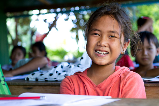 A young Asian girl is smiling in a classroom.