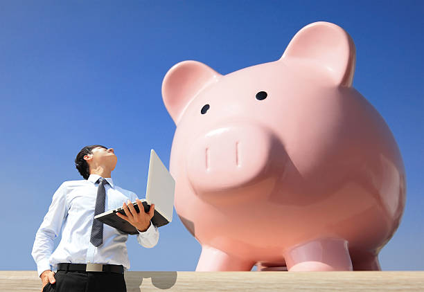 Saving Money with my piggy bank - Young business man look to piggy bank with computer
