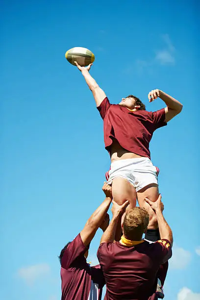 A rugby player being lifted up and catching the ball