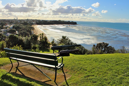Stunning view of Auckland's North Shore from North Head Historic Reserve, Devonport.  Empty bench, gun's left over from coastal defense during the war, popular Cheltenham Beach, Rangitoto shipping channel, suburbs and coast line all the way north
