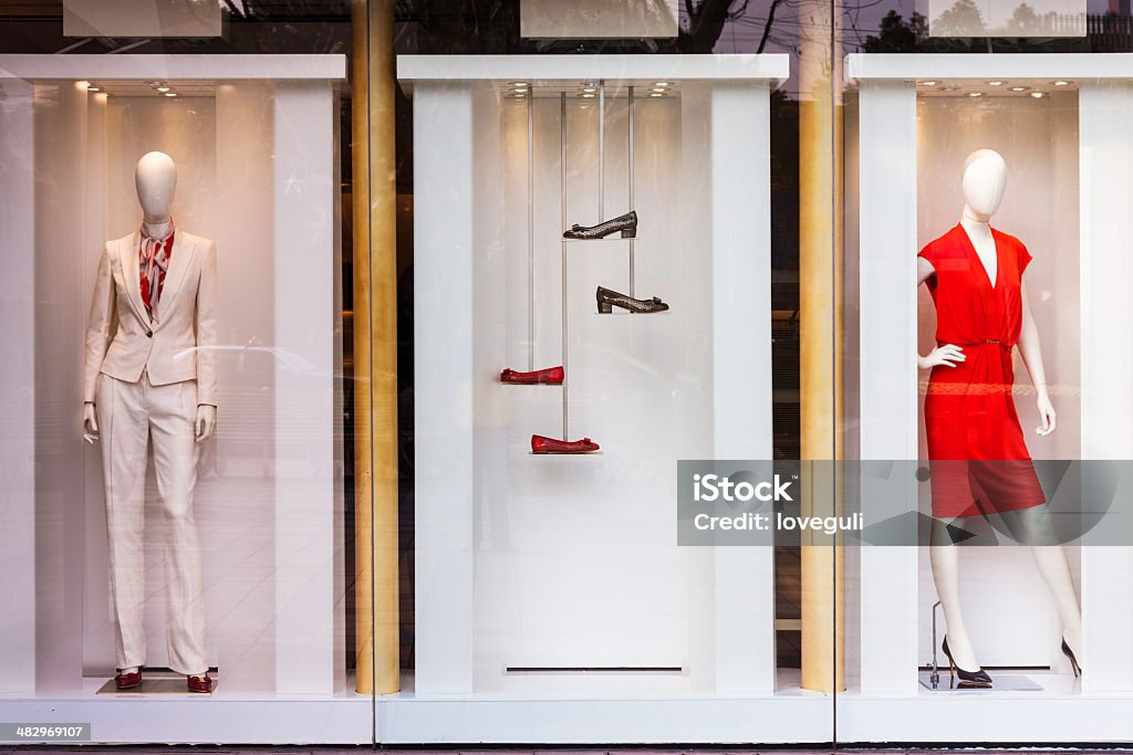 Boutique window with shoes, bags and mannequin Three display windows, with the middle one showing two pairs of women's shoes suspended from the ceiling.  The other windows each contain a female mannequin, with one wearing a cream-colored suit and the other a red dress. Mannequin Stock Photo