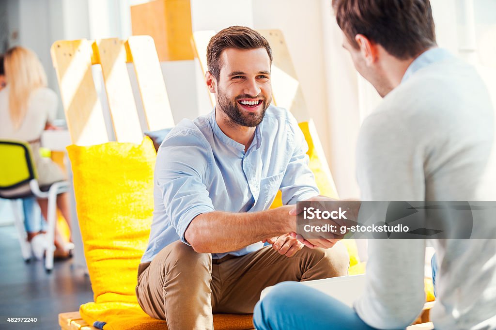 Sealing a deal! Two happy young men shaking hands while sitting in the rest area of the office Handshake Stock Photo