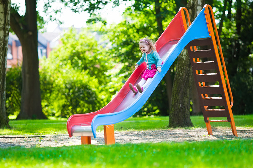 Little girl on a playground. Child playing outdoors in summer. Kids play on school yard. Happy kid in kindergarten or preschool. Children having fun at daycare play ground. Toddler on a slide.