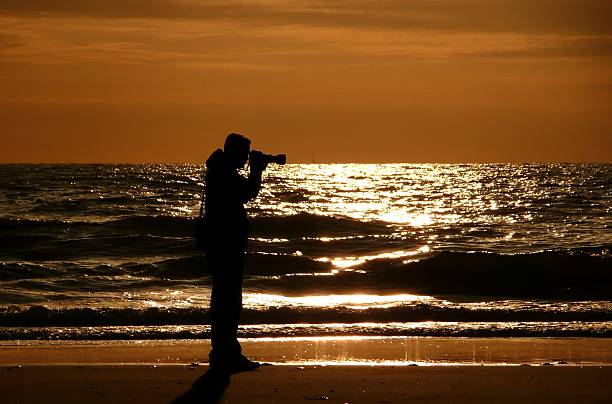 Senior European tourist photographing on the Legzira beach, on the shores of the Adriatic Ocean, Sidi Ifni Province, southwest Morocco, Africa. He is standing, walking in the shallow water, he is using a tripod. Nikon D800, full frame, XXXL.