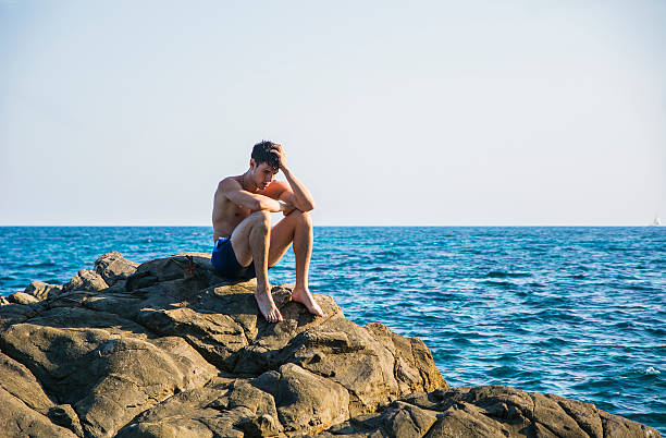 istock Muscular young man on rock by sea 482987184