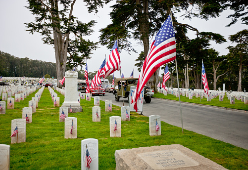 San Francisco, USA - May 27, 2013: US Memorial Day Ceremony, The Presidio National Cemetery, San Francisco.   The Ceremony was also dedicated to the 60th Anniversary of Korean War (1950-1953) remembering and honoring more than 50.000 Americans killed during that war. Graves are decorated with American Flags, old cars parked on cemetery. 