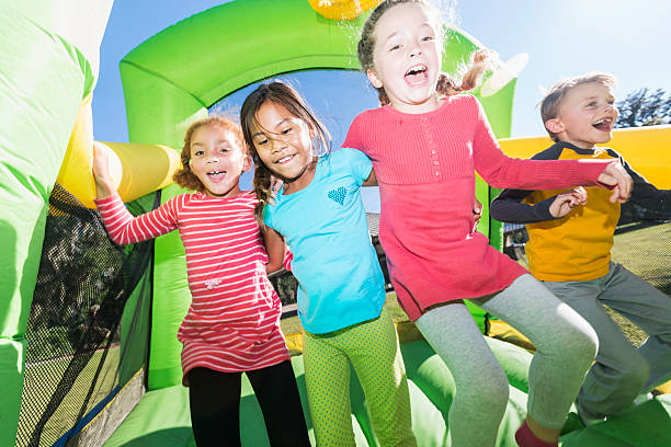 vier multikulturellen kinder springen auf der hüpfburg - house bouncing multi colored outdoors stock-fotos und bilder
