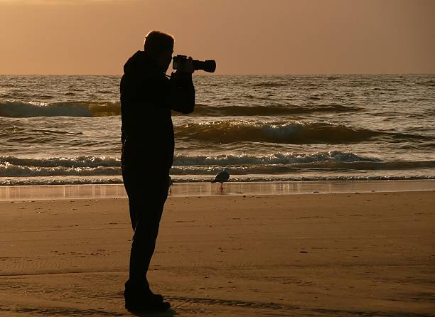 istock Backlight silhouette of photographer standing upon the foreshore. 482988764