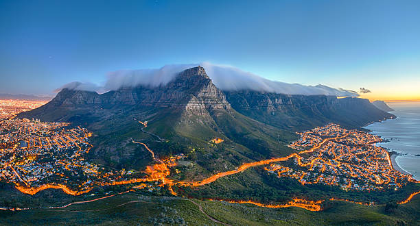 Table Mountain, Cape Town, South Africa Table Mountain covered by its typical cloud table cloth and the twelve Apostles. Below on the left you can see Cape Town and the beautiful Camps Bay on the right. Taken right after sunset. southern africa stock pictures, royalty-free photos & images