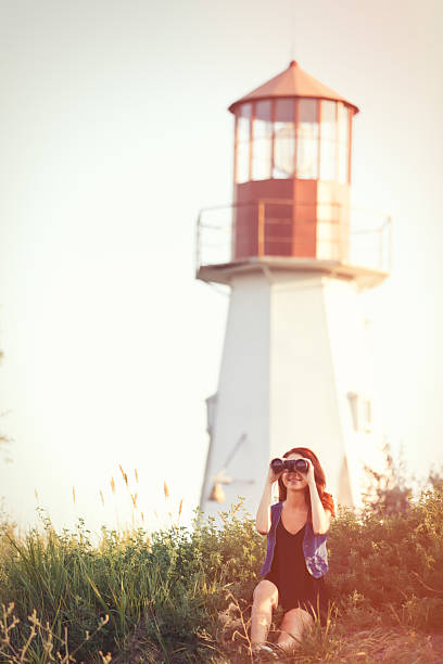 girl with binocular sitting on the grass near Lighthouse