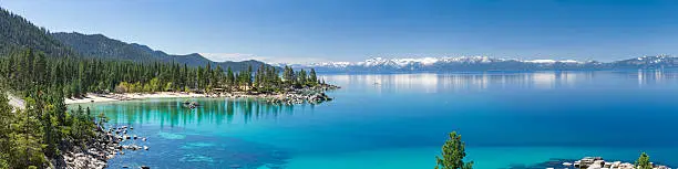 This is a high resolution panorama of Lake Tahoe near Sand Harbor. This is east shore line with many rocks and pine trees photographed in the morning during summer. Sierra Nevada mountains with snowy peaks reflecting in lake turquoise waters.