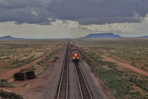 A train crosses the vast expanse of Eastern Arizona through approaching storms , about to cross under a bridge which offered this unique higher-angle perspective. 