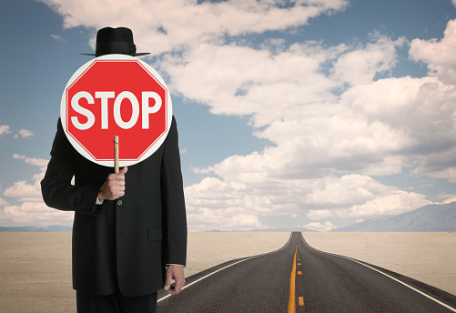 A businessman standing on a long open highway holding a Stop sign.