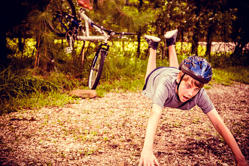 Young teenager having mountain bike accident while riding through trees to rural road.  Cross processed. 