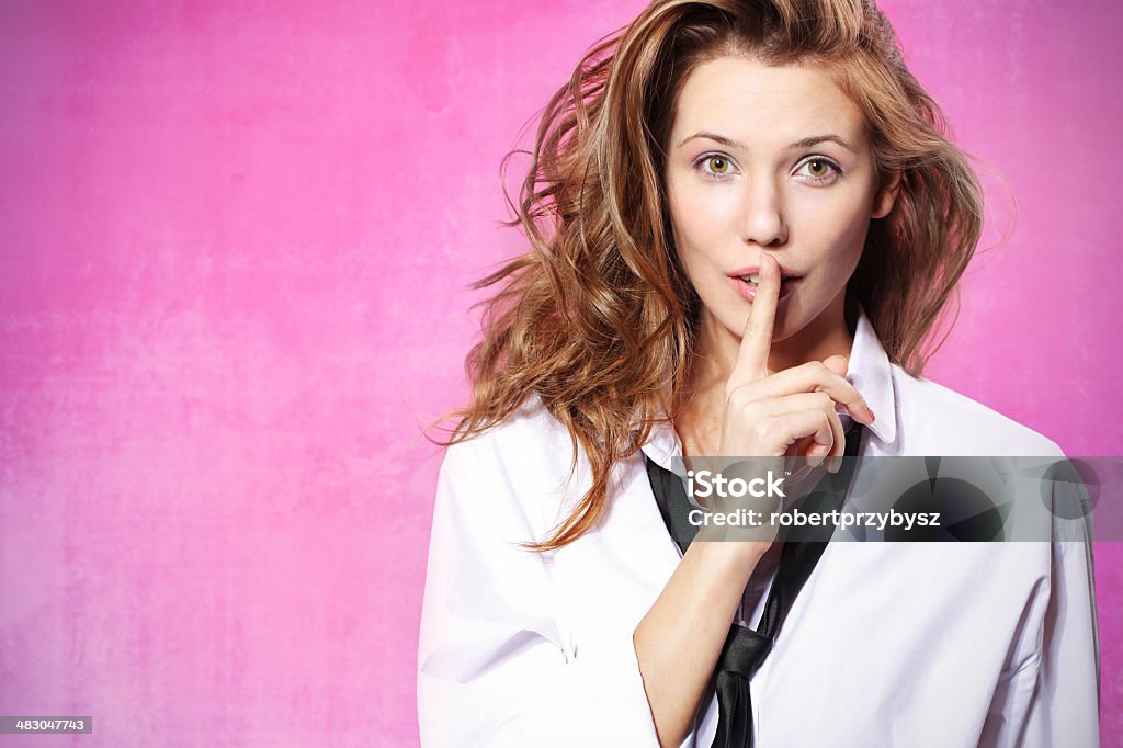 Hush, it's a secret! Young woman covering her mouth with your finger on a pink background standing in front of the lens.  Blond Hair Stock Photo