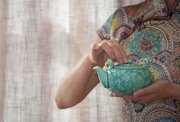 Chinese woman wearing QiPao holding a porecelain teapot