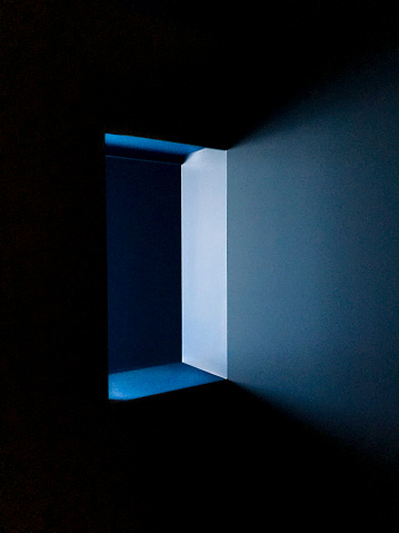 Blue light shining through a window opening in a dark roon.