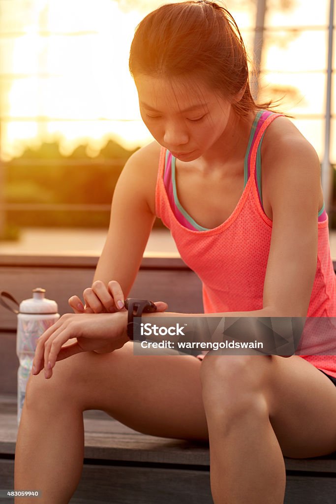 fitness wearable technology sporty asian chinese woman sitting outdoors checking workout time on wearable technology watch after run 2015 Stock Photo