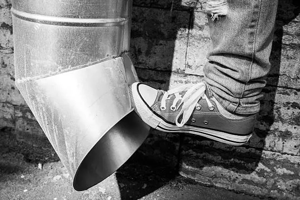 Teenager in sneakers kicks drainpipe, black and white urban photo