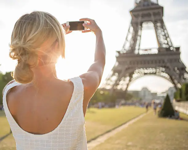 Photo of Cheerful young woman photographing Eiffel tower using mobile phone