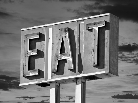 Vintage black and white eat sign with sunset sky.