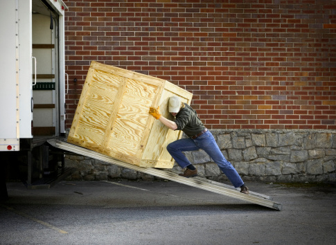 A courier pushing a crate up a ramp into a delivery truck.