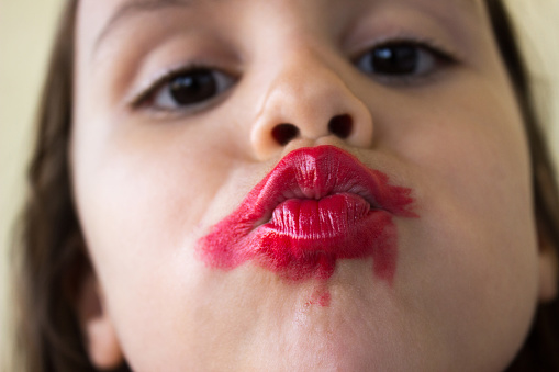 Little girl kissing with messy lipstick. Close up portrait. Horizontal composition. Image developed from Raw format.