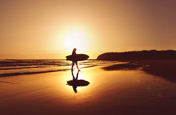 Silhouette of surfer walking off beach with surfboard stock photo