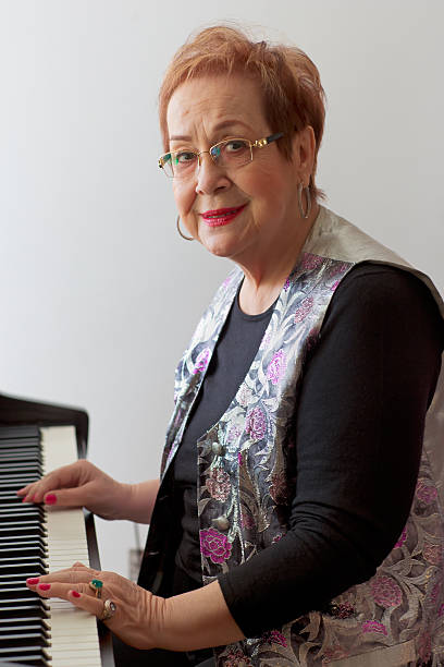 A young and beautiful girl smiling, sitting at the piano with a blurred score and looking at the camera