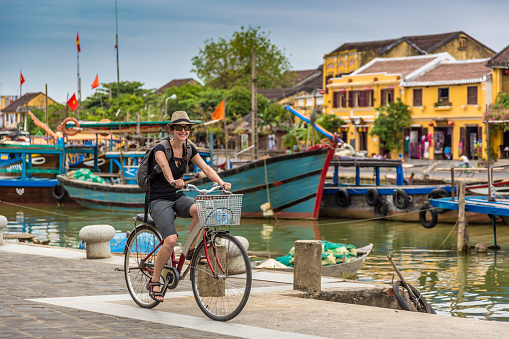 Woman Tourist Cycling in Hoi An City, Vietnam. She is happy and smiling and the coloured buildings of the city are in the background.