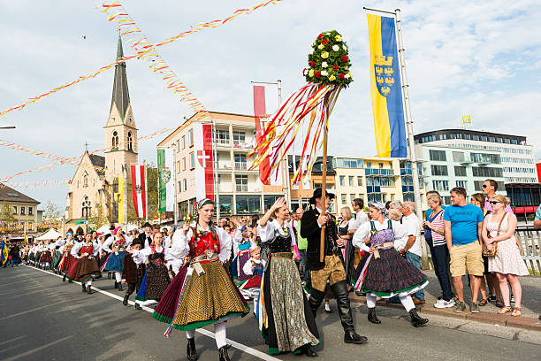 Villach Church Day Villach, Austria - August 1, 2015: On the main bridge over Drava River the costume parade - man and women in national costume parading past many spectators on sides applauding and taking photos. Houses and cathedral in background and provincial flags.  villach stock pictures, royalty-free photos & images