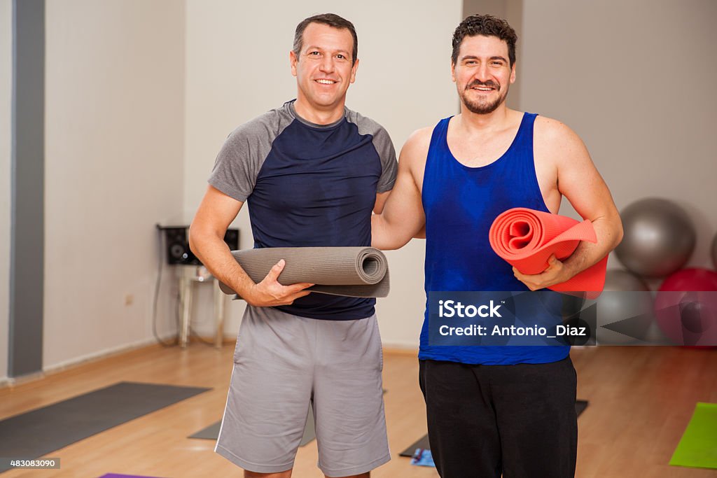 Male friends ready for yoga class Portrait of a couple of guys carrying exercise mats and smiling in a yoga studio Gym Stock Photo