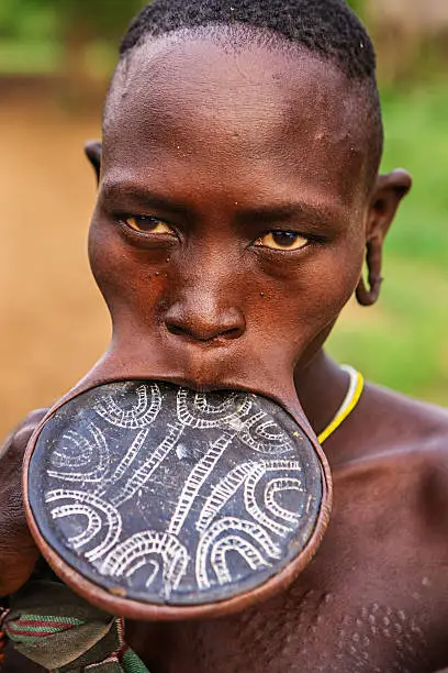 Woman from Mursi tribe holding her baby.  Mursi tribe are probably the last groups in Africa amongst whom it is still the norm for women to wear large pottery or wooden discs or ‘plates’ in their lower lips.http://bem.2be.pl/IS/ethiopia_380.jpg