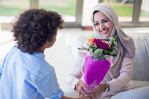 Middle Eastern boy giving flowers to his mother, mother looks happy to his son.