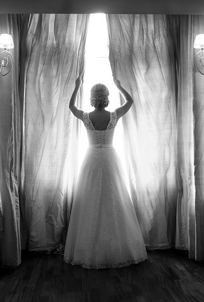 vue arrière de la mariée posant sur grande fenêtre dans la chambre à coucher - wedding dress wedding domestic room bride photos et images de collection