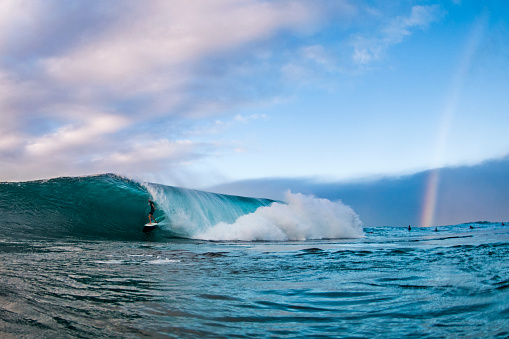 A professional surfer rides through a perfect North Shore barrel as a rainbow shines in the background