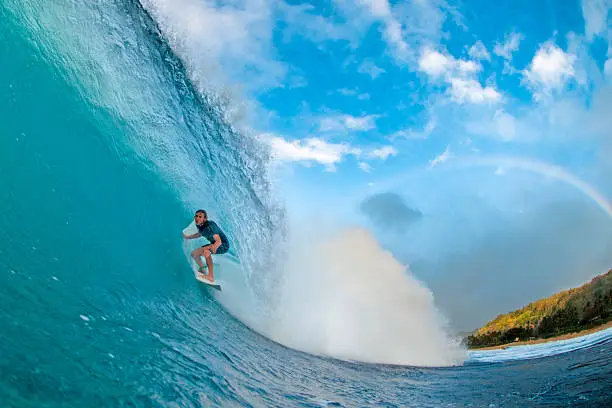 A professional surfer rides a perfect North Shore barrel with a rainbow in the background
