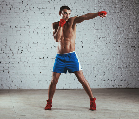 Professional boxer standing against brick wall and throwing jab.