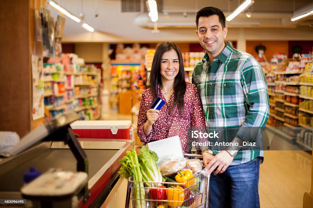 Using a credit card at the store Cute happy couple paying for their food at the checkout counter with a credit card Credit Card Stock Photo