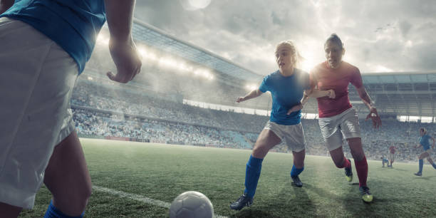 Women Soccer Players in Mid Match Action A mid action image of two professional women soccer players pushing on each other to compete for possession of the football. The action takes place during a soccer game in generic outdoor a floodlit soccer stadium full of spectators under an overcast evening sky. Both players are wearing generic unbranded soccer kit.  womens soccer stock pictures, royalty-free photos & images