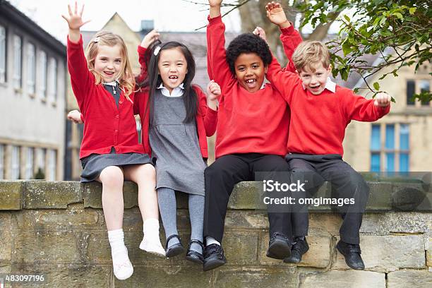 Portrait Of School Pupils Sitting On Wall Together Stock Photo - Download Image Now - Children Only, Looking At Camera, Sitting