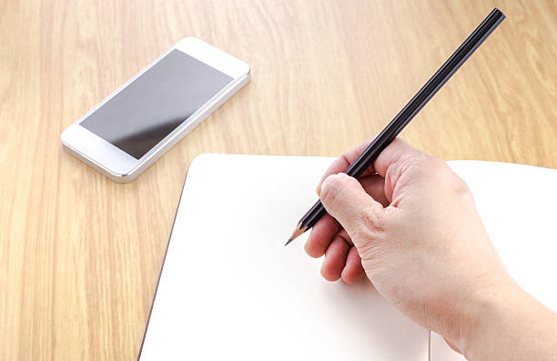 istock Hand holding pencil writing on blank notebook with smartphone 483098356