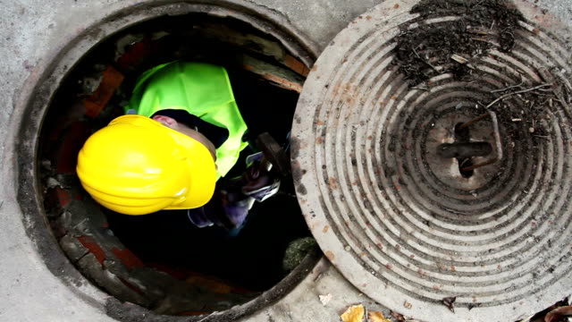 Manhole Workers Passing Each Other a Hammer