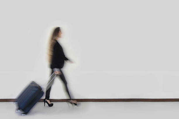 Young businesswoman walking while carrying wheeled luggage in front of a corporate building at night. Close-up.