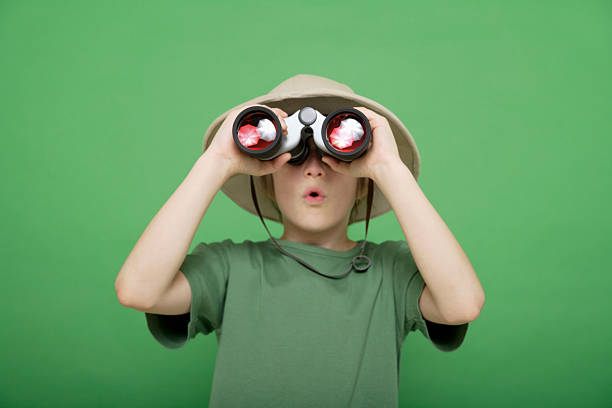 緑色の背景に対して双眼鏡を通して見ている少年 - 探求 ストックフォトと画像