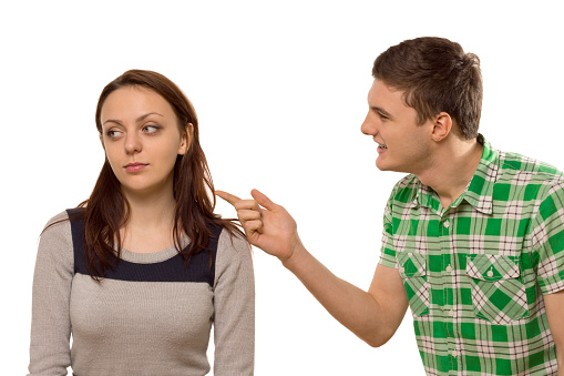Young man arguing with his girlfriend pointing his finger at her as she turns aside in indifference, isolated on white