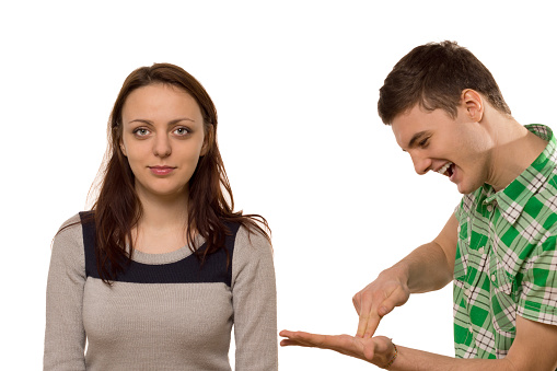 Enthusiastic young man explaining something to his girlfriend gesturing on his hand as she listens with an amused but disinterested expression, isolated on white
