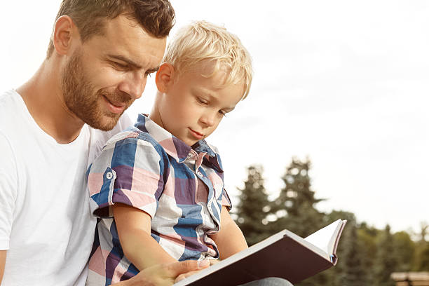istock Father and son reading book in park 483128696