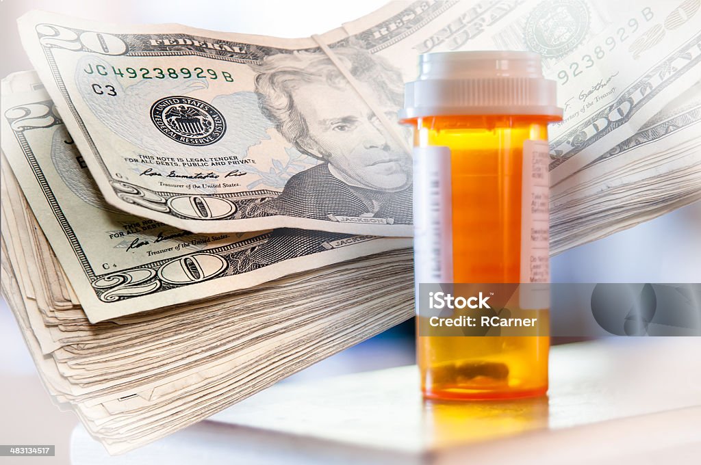 Medicine Bottles and Money Medicine bottles and a stack of twenty dollar bills with white vignette Bottle Stock Photo